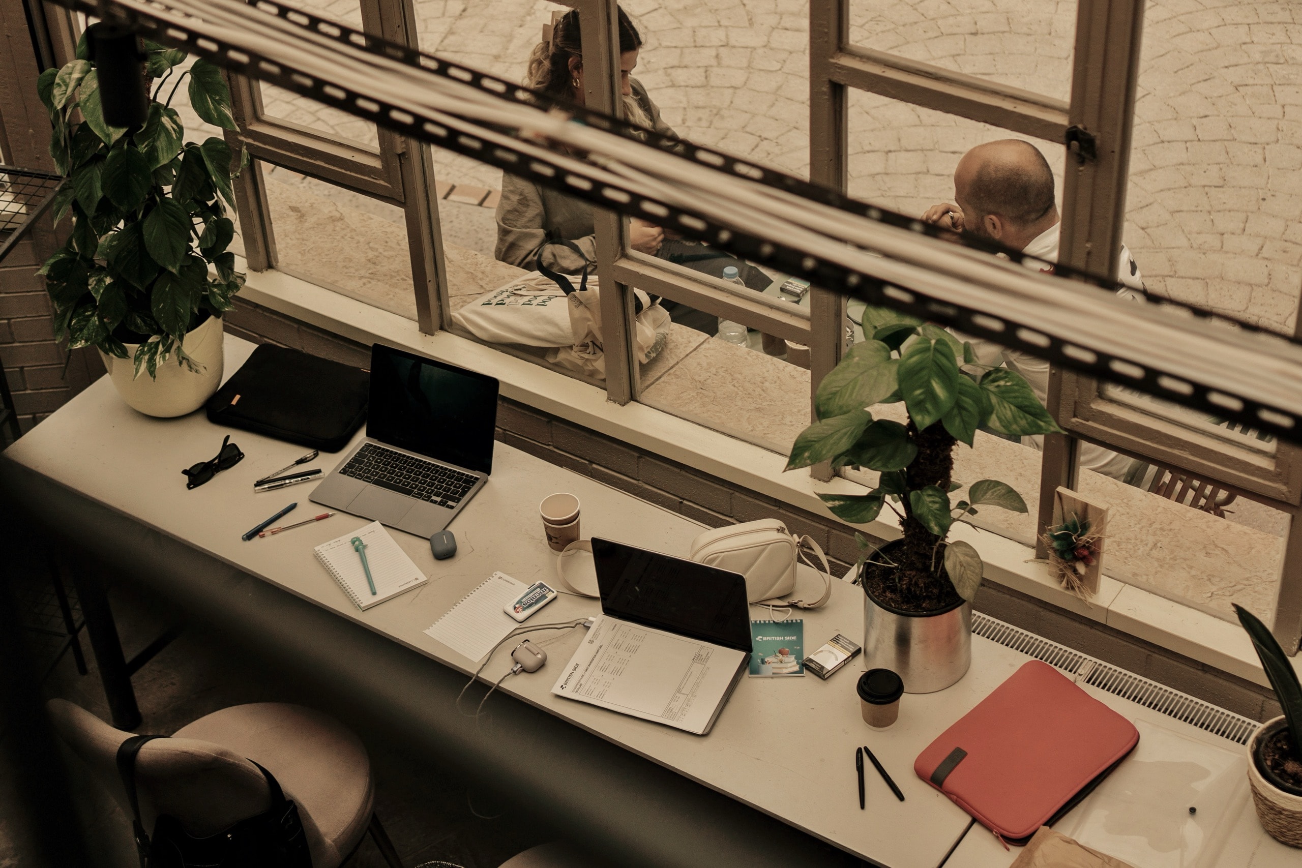 A reporter's desk by the window at golden hour — laptops open, a notebook and pen, coffee going cold, the day's work in progress.